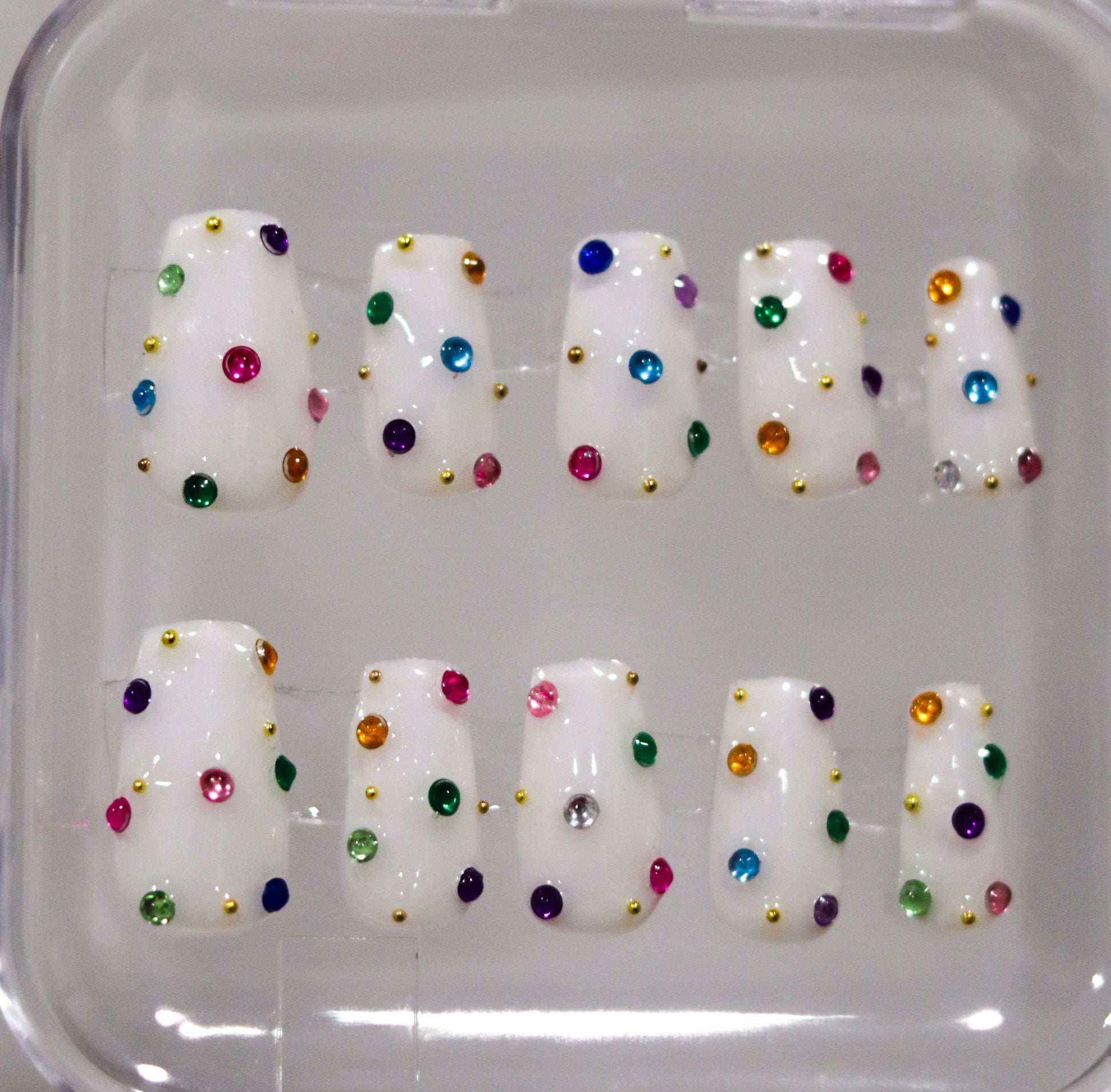 Set of white nail tips with colorful dots in a clear case.
