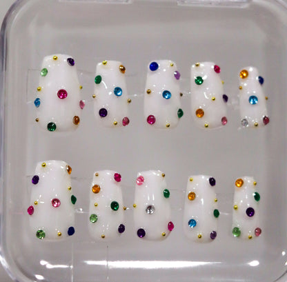 Set of white nail tips with colorful dots in a clear case.